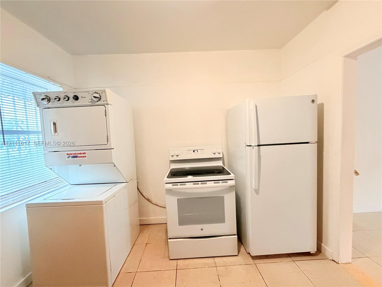 Stacked washer and dryer unit, electric range, and top-freezer refrigerator set upon tile flooring