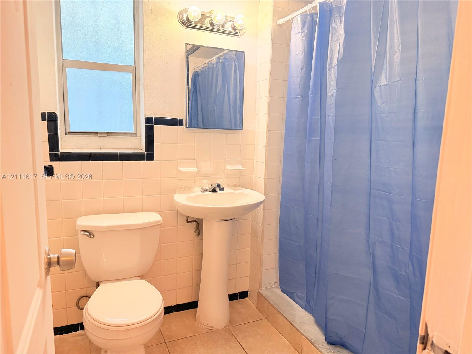 Bathroom featuring a pedestal sink, wall-mounted medicine cabinet, tri-light vanity fixture, and white wall tile with dark decorative accent trim