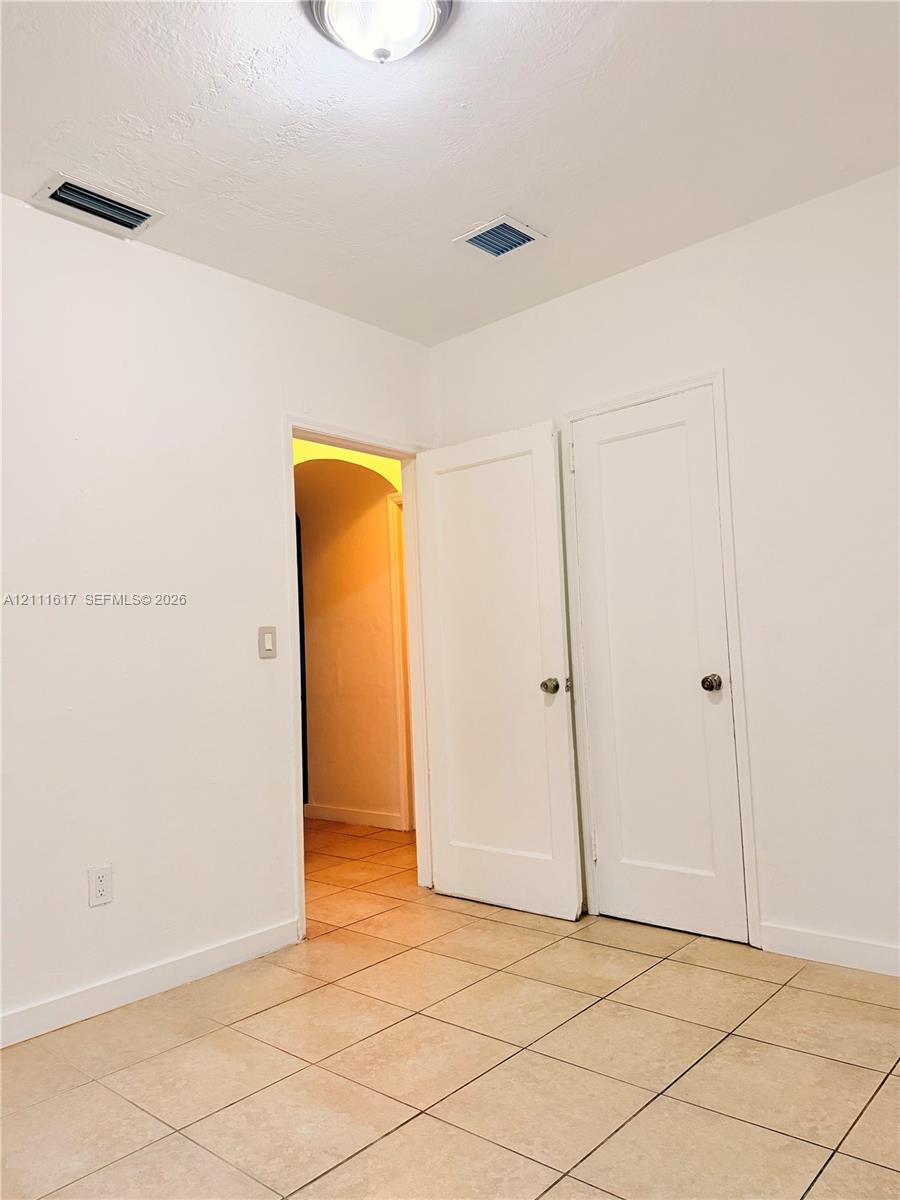 Room with neutral tile flooring, two solid-core interior doors, and arched entryway