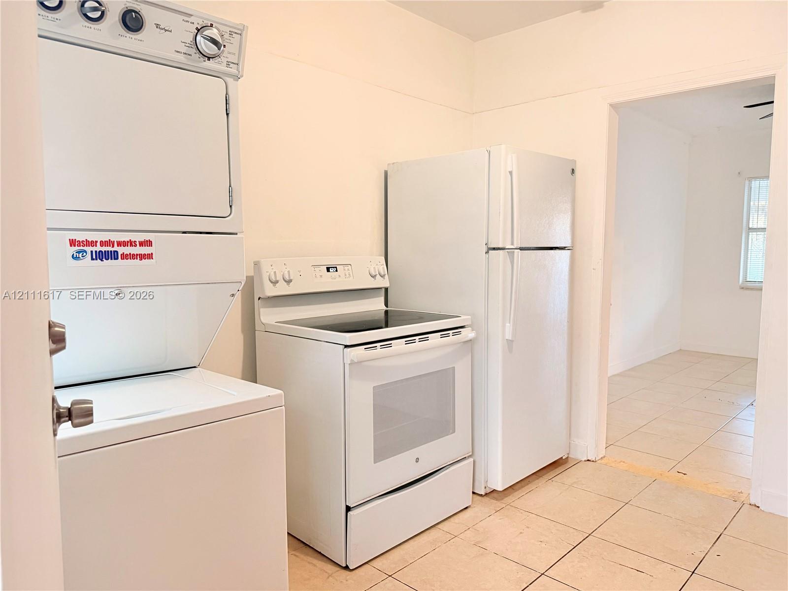 Stacked laundry unit, white electric range, and full-size refrigerator, featuring tile flooring
