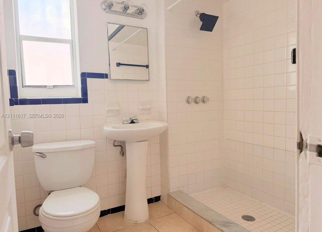 Bathroom featuring a white ceramic pedestal sink, tiled shower enclosure, square wall mirror, and chrome finish hardware