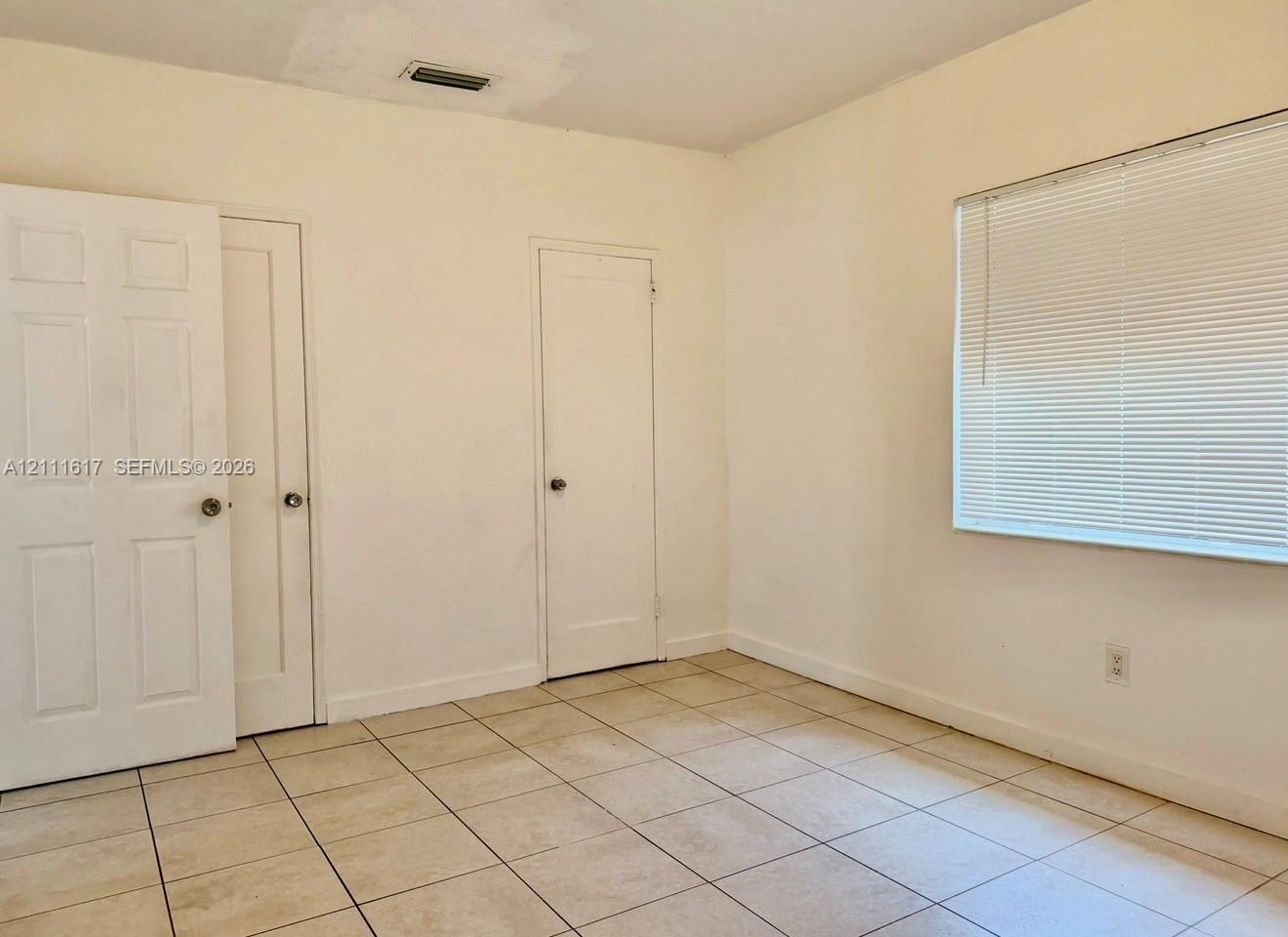 Room featuring neutral wall finishes, tile flooring, two solid-core interior doors, and a window fitted with horizontal blinds