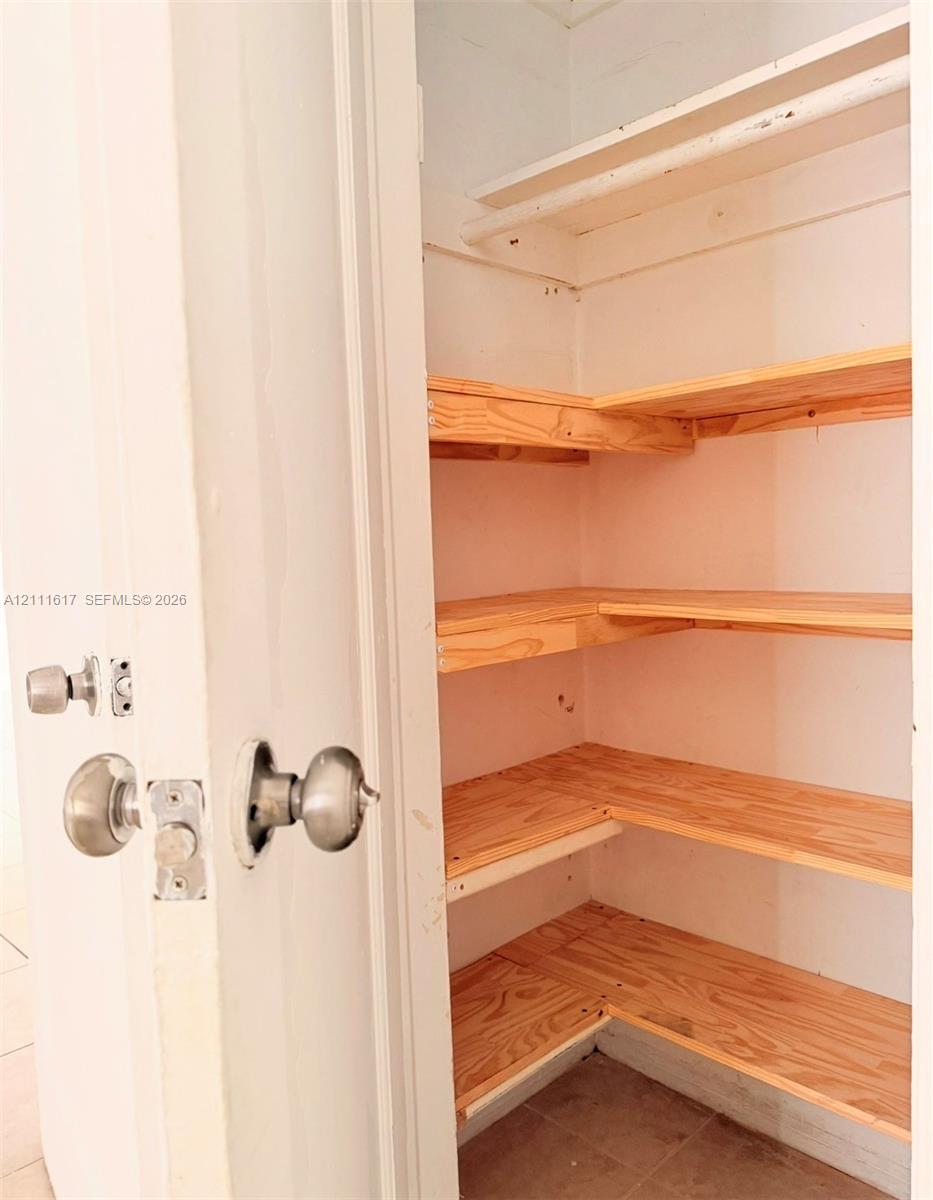 Storage closet featuring multi-level wooden shelving, a built-in overhead shelf with hanging rod, and brushed metal door hardware