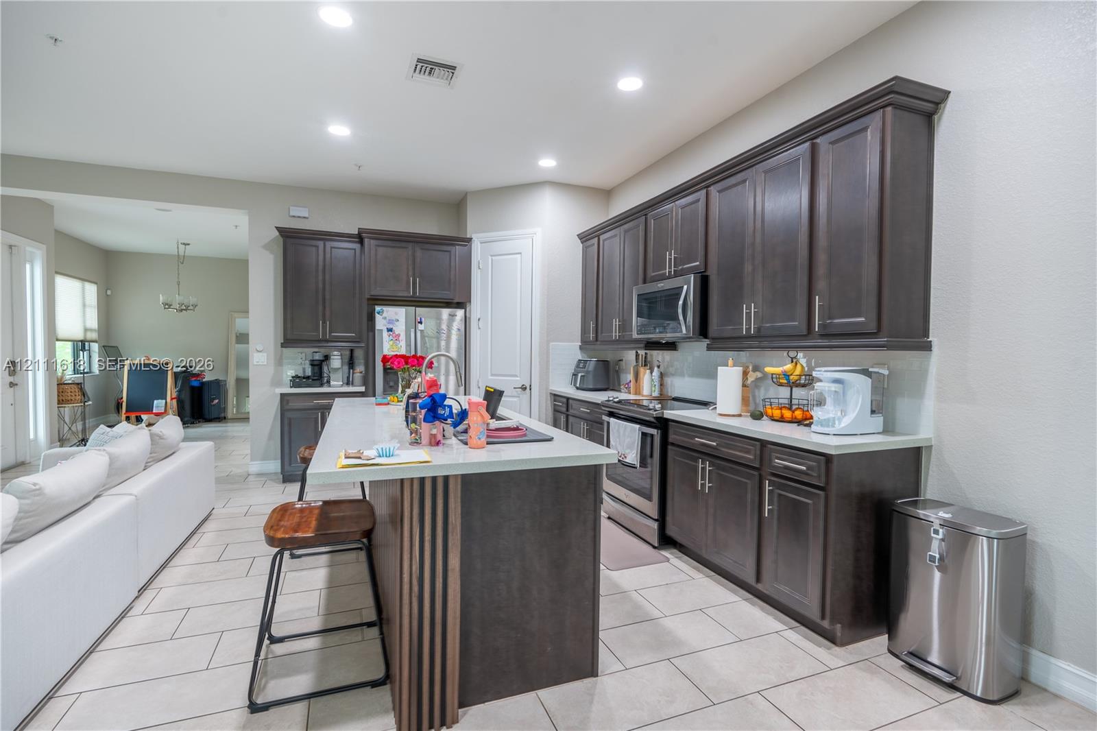 Kitchen featuring dark wood cabinetry, a central island with a stone-finish countertop, recessed lighting, and tile flooring