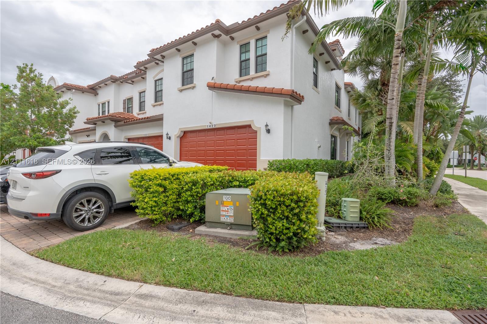 Stucco exterior featuring red-tiled roof accents, paver driveway, and attached two-car garage