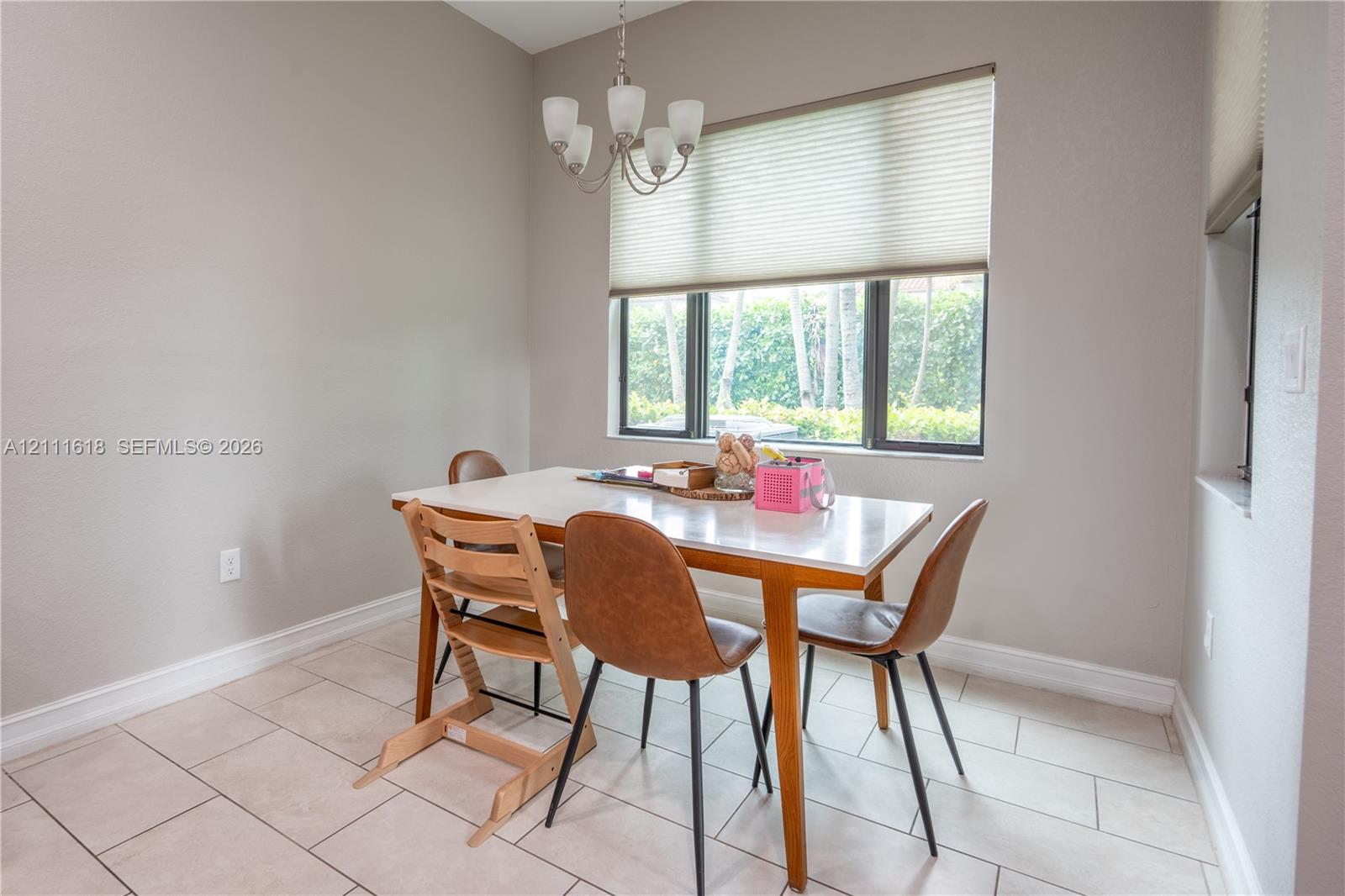 Multi-light chandelier, neutral ceramic tile flooring, and large window with integrated blinds