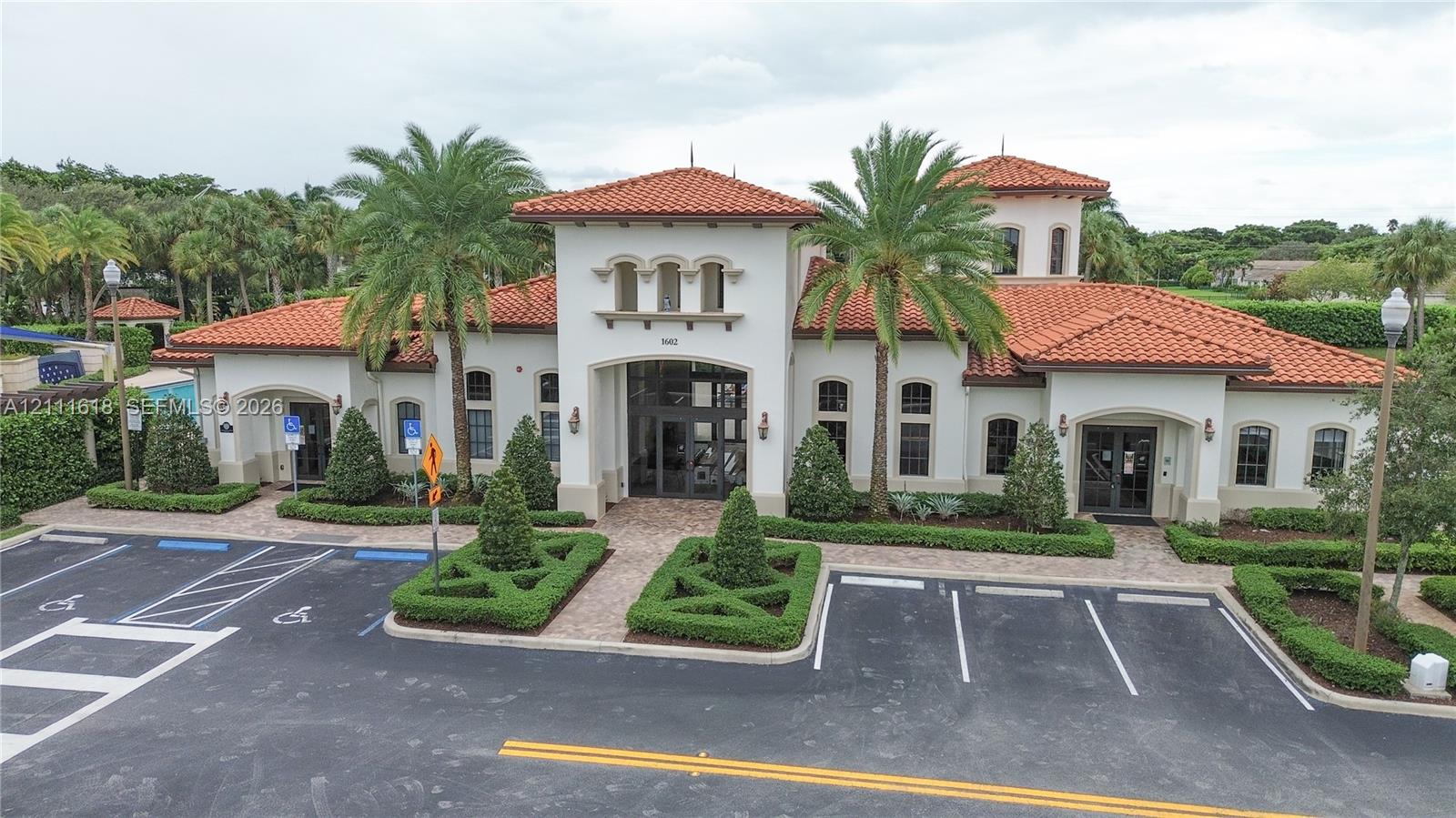 Mediterranean-style exterior featuring a terra-cotta tile roof, stucco facade, arched windows, and manicured landscaping
