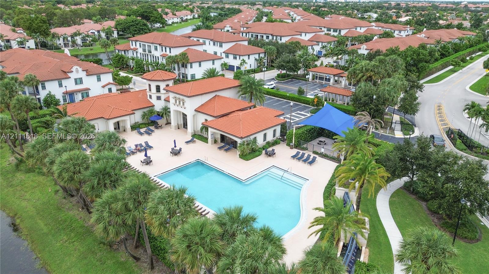 Community swimming pool featuring a paved deck, terracotta tile roof clubhouse, and extensive landscaping with palm trees