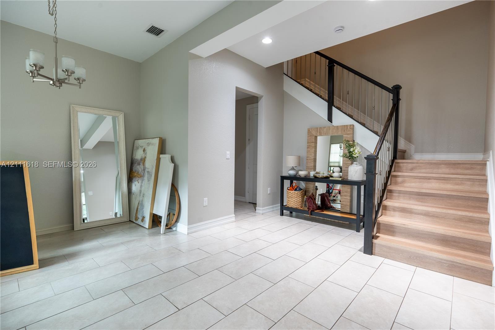 Foyer featuring large-format ceramic tile flooring, a staircase with wood-finish treads, a black metal balustrade, recessed lighting, and a multi-arm pendant fixture