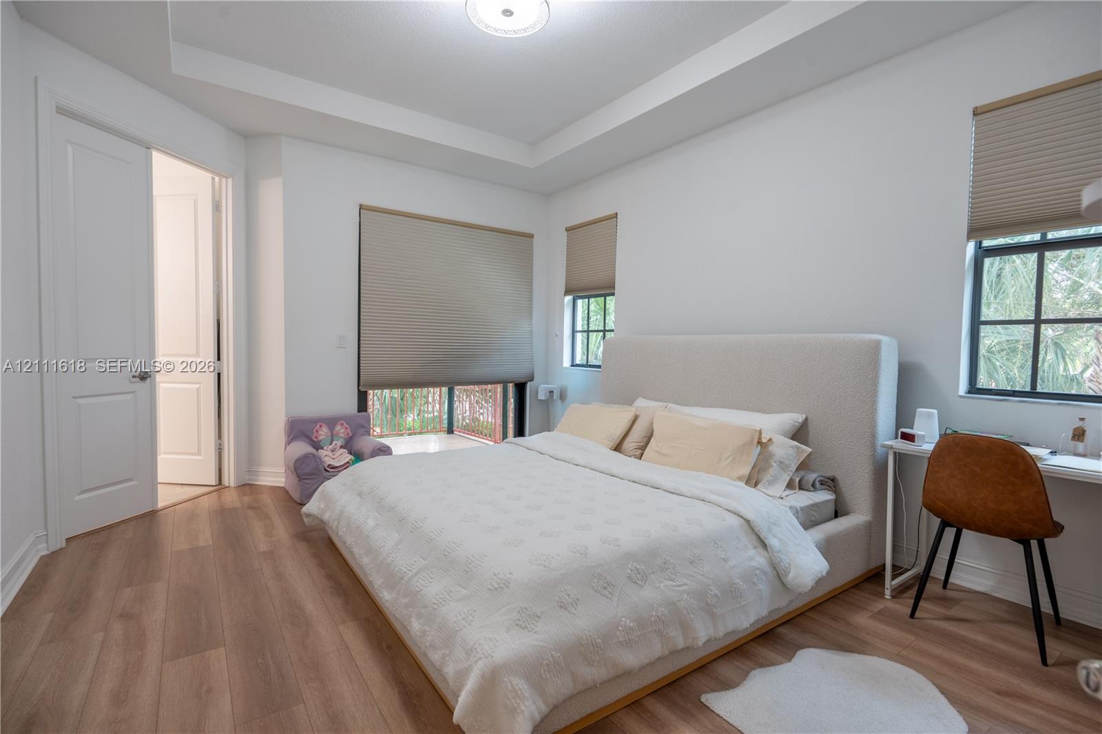 Bedroom featuring a tray ceiling, wood-finish flooring, multi-pane windows with integrated shades, and a solid-core interior door