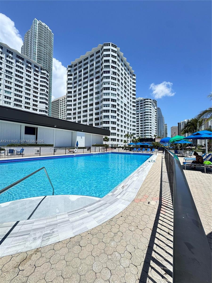 Outdoor swimming pool featuring a concrete paver deck, metal perimeter fencing, and a metal handrail