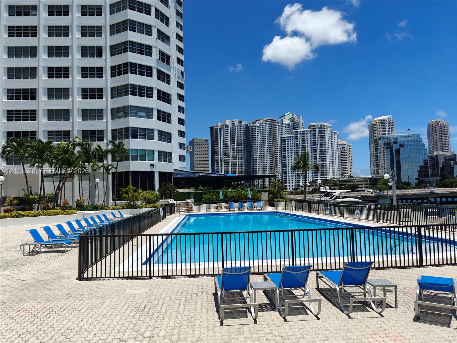 Swimming pool with paved surround, secured metal perimeter fencing, and established palm trees