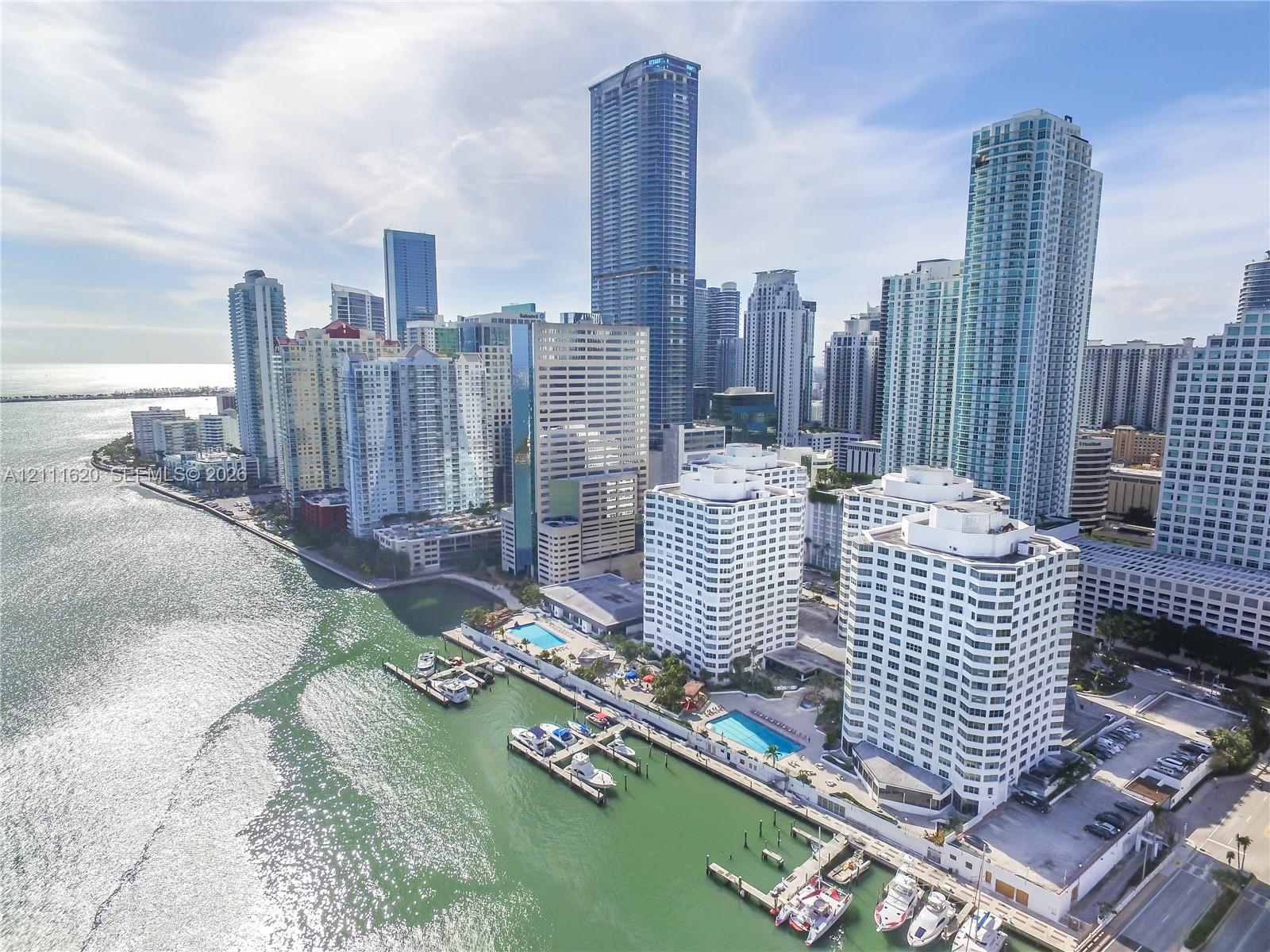 Aerial perspective of a high-rise residential complex featuring waterfront access, private boat slips, outdoor swimming pools, and extensive hardscaped terrace areas