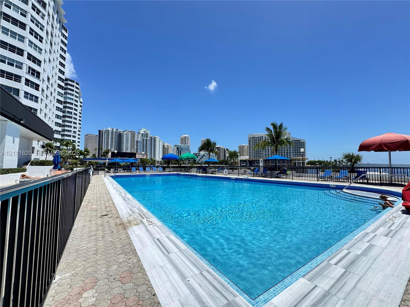 Swimming pool with tiled decking, metal perimeter fencing, and stone-surfaced pool coping