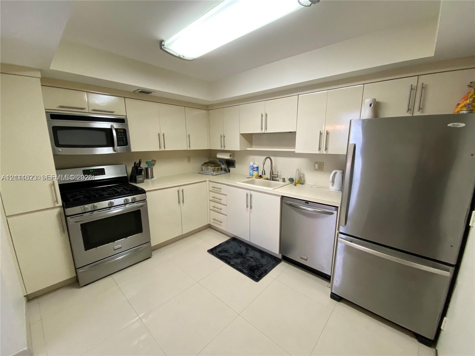 Kitchen featuring high-gloss cabinetry, stainless steel appliances, solid-surface countertops, and tile flooring