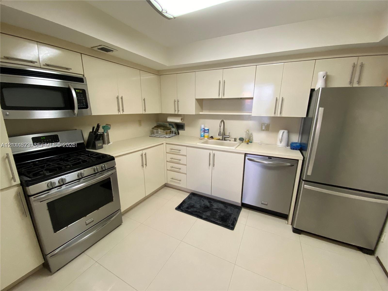 Kitchen featuring high-gloss cabinetry, stainless steel appliances, solid-surface countertops, and tile flooring