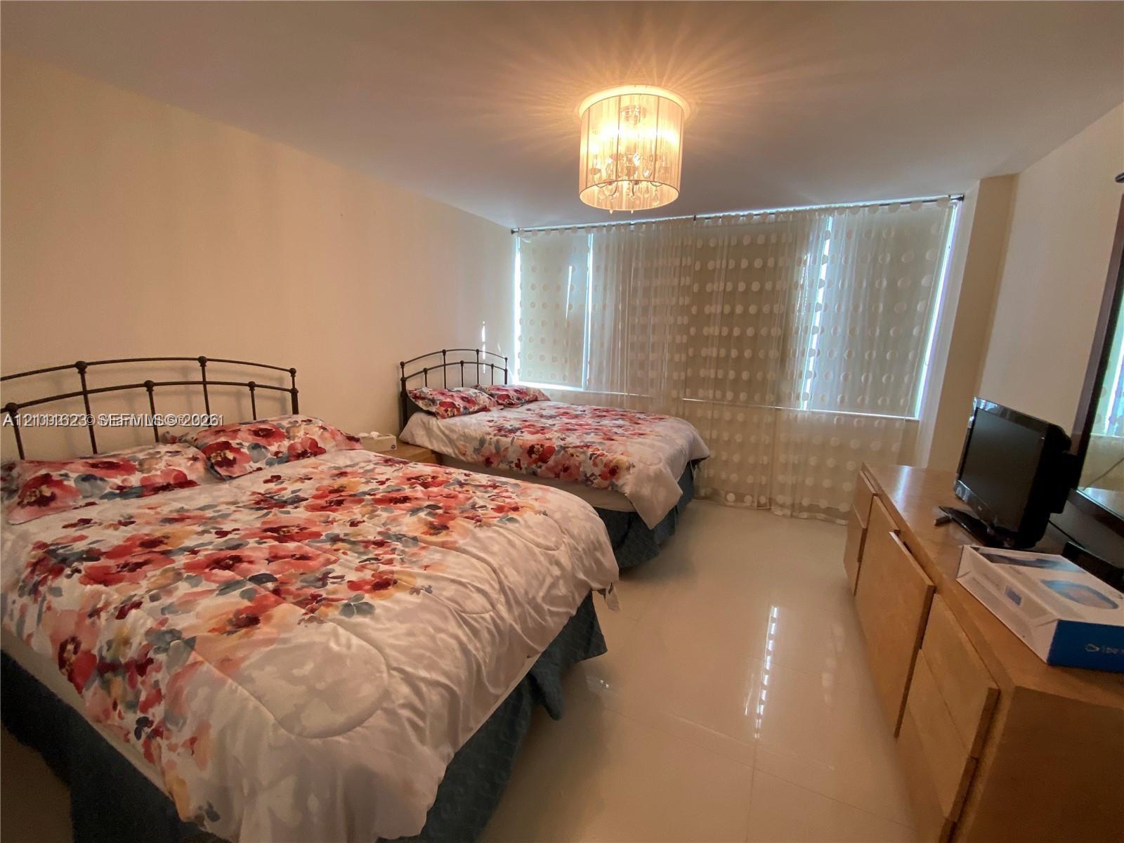 Spacious room featuring floor-to-ceiling windows with vertical blinds, glossy tile flooring, and a tiered crystal chandelier
