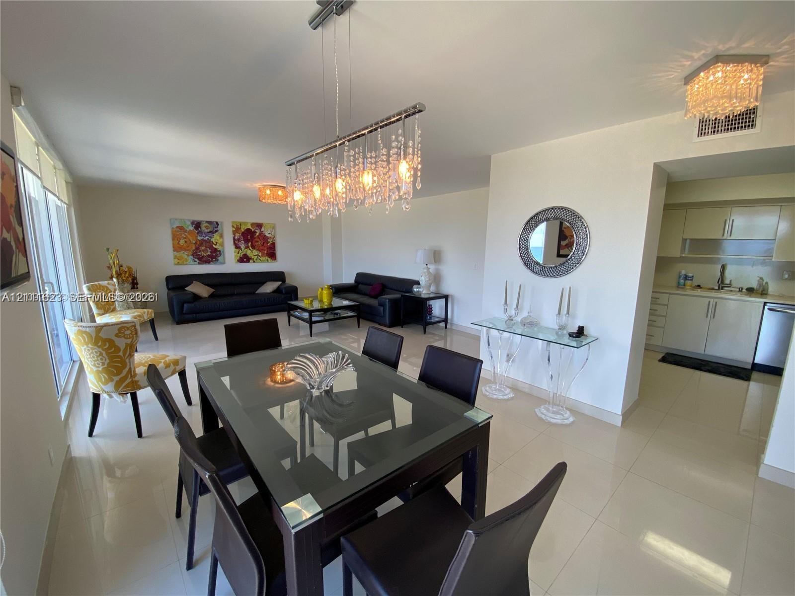 Open-concept living space featuring large-format tile flooring, a linear crystal chandelier, recessed lighting, and a kitchen equipped with flat-panel cabinetry