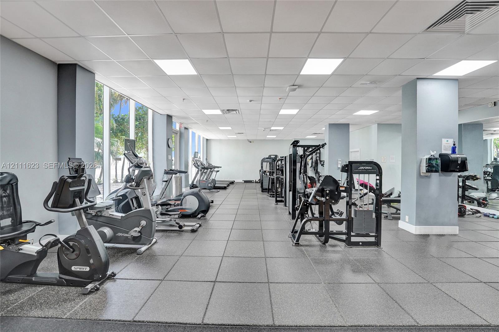 Fitness center featuring floor-to-ceiling windows, professional rubber tile flooring, and integrated wall mirrors