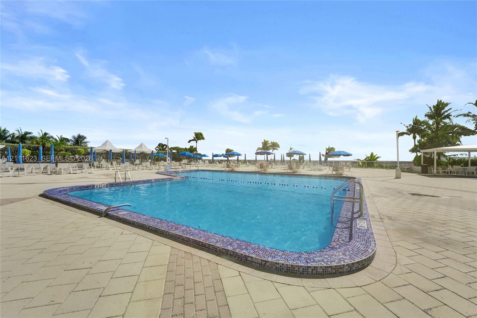 Swimming pool with mosaic tile border, metal handrails, and paved deck surround