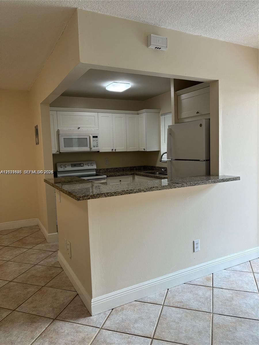 Kitchen featuring white cabinetry, stone countertops, a breakfast bar, and tile flooring