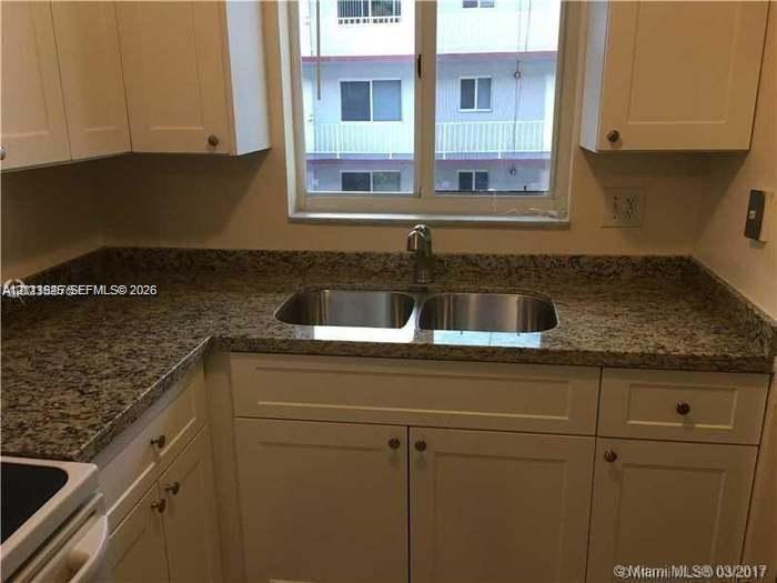 Kitchen featuring shaker-style cabinetry, stone-patterned countertops, dual-basin stainless steel sink, and a window-mounted faucet