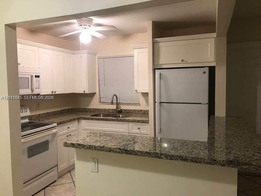 Kitchen featuring white cabinetry, stone-finish countertops, an integrated pass-through counter, a dual-basin sink with a gooseneck faucet, and tile flooring
