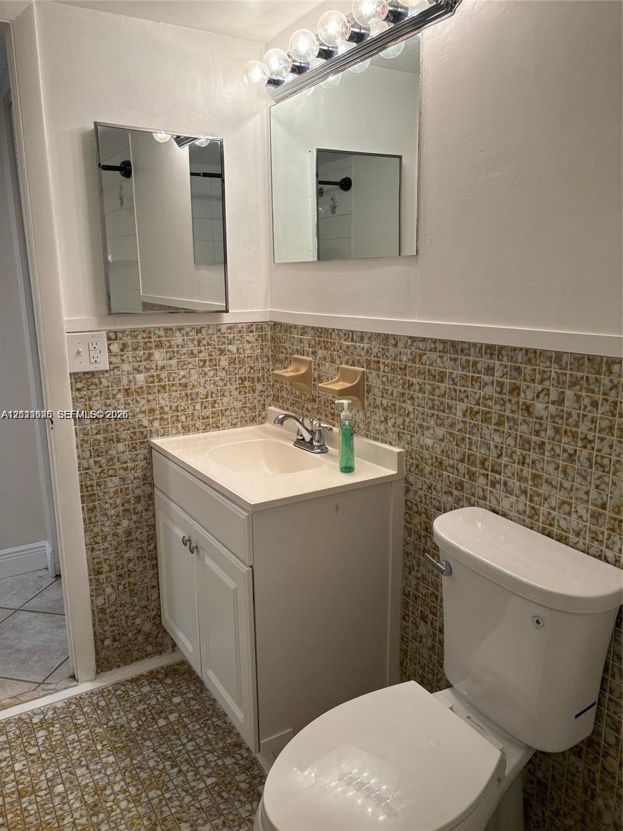 Bathroom featuring a single-sink vanity with a solid-surface countertop, mosaic tile backsplash, two wall-mounted mirrors, and multi-bulb vanity lighting