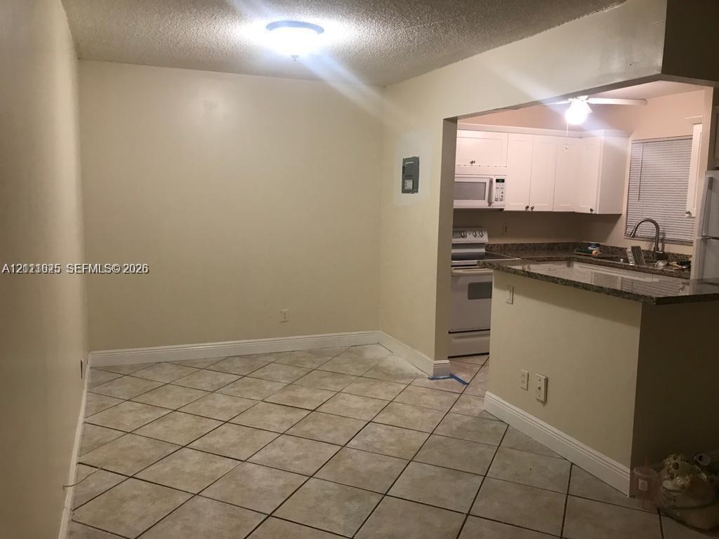 Ceramic tile flooring, white cabinetry, integrated microwave, stone-finish countertops, and a kitchen peninsula