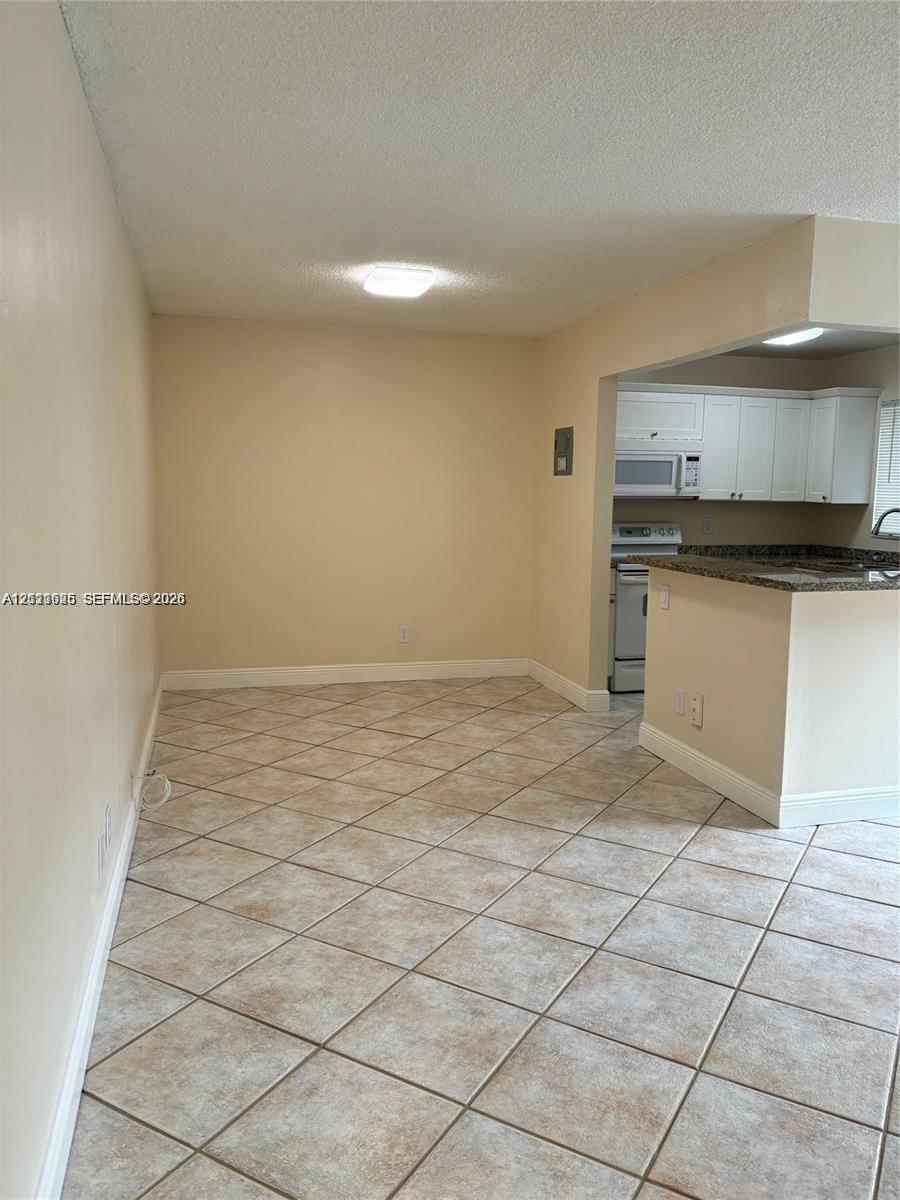 Ceramic tile flooring, kitchen featuring a breakfast bar, white cabinetry, built-in microwave, and stone-finish countertops