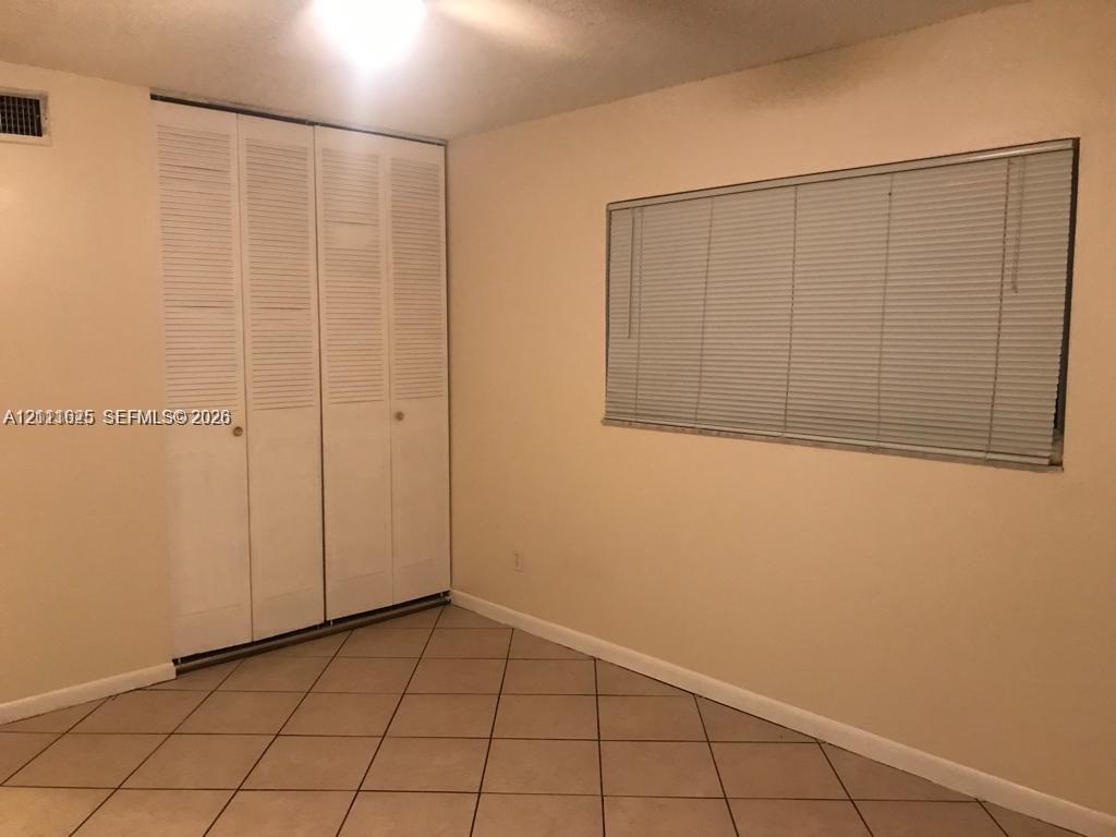 Neutral-toned room featuring tiled flooring, a set of floor-to-ceiling bi-fold closet doors, and a rectangular window fitted with horizontal blinds
