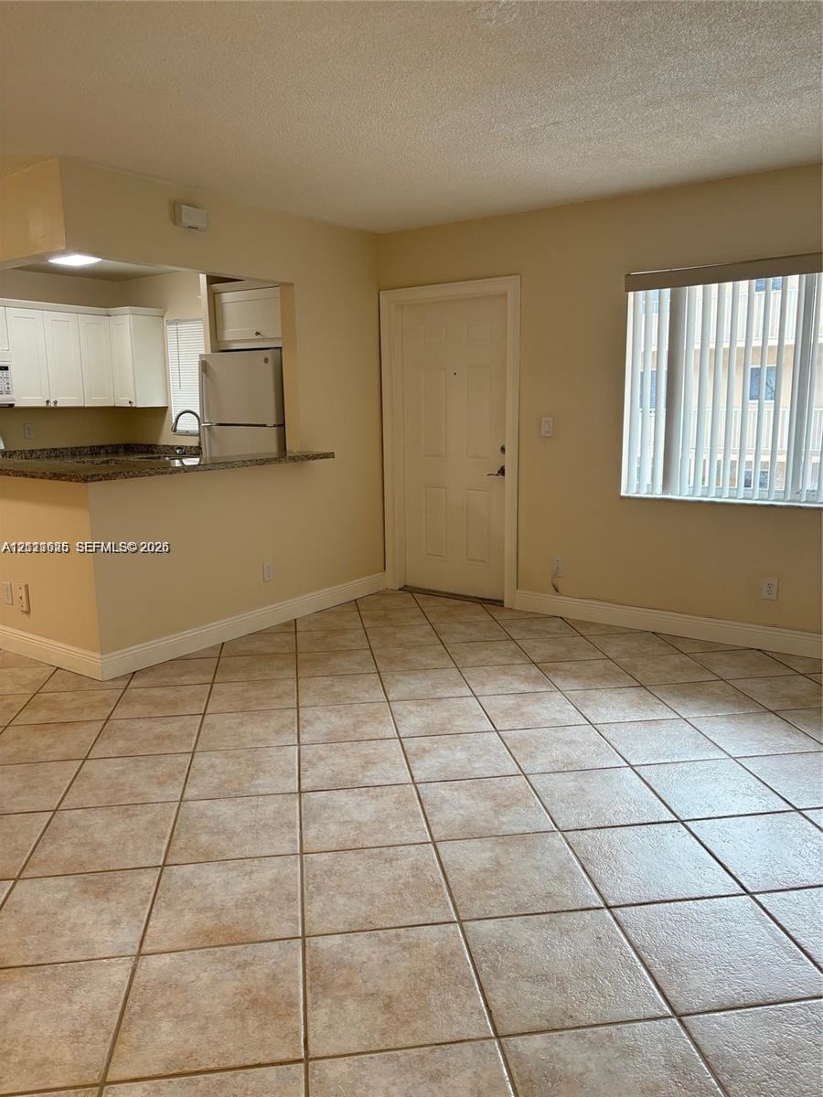 Open-concept kitchen featuring white cabinetry and stone-finish countertops, complemented by large-format tile flooring and vertical window blinds