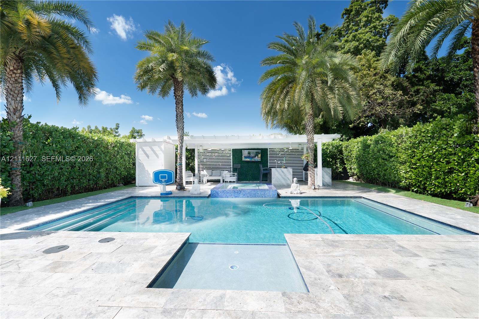 Swimming pool with built-in spa, stone paver patio, covered cabana, and perimeter privacy hedges