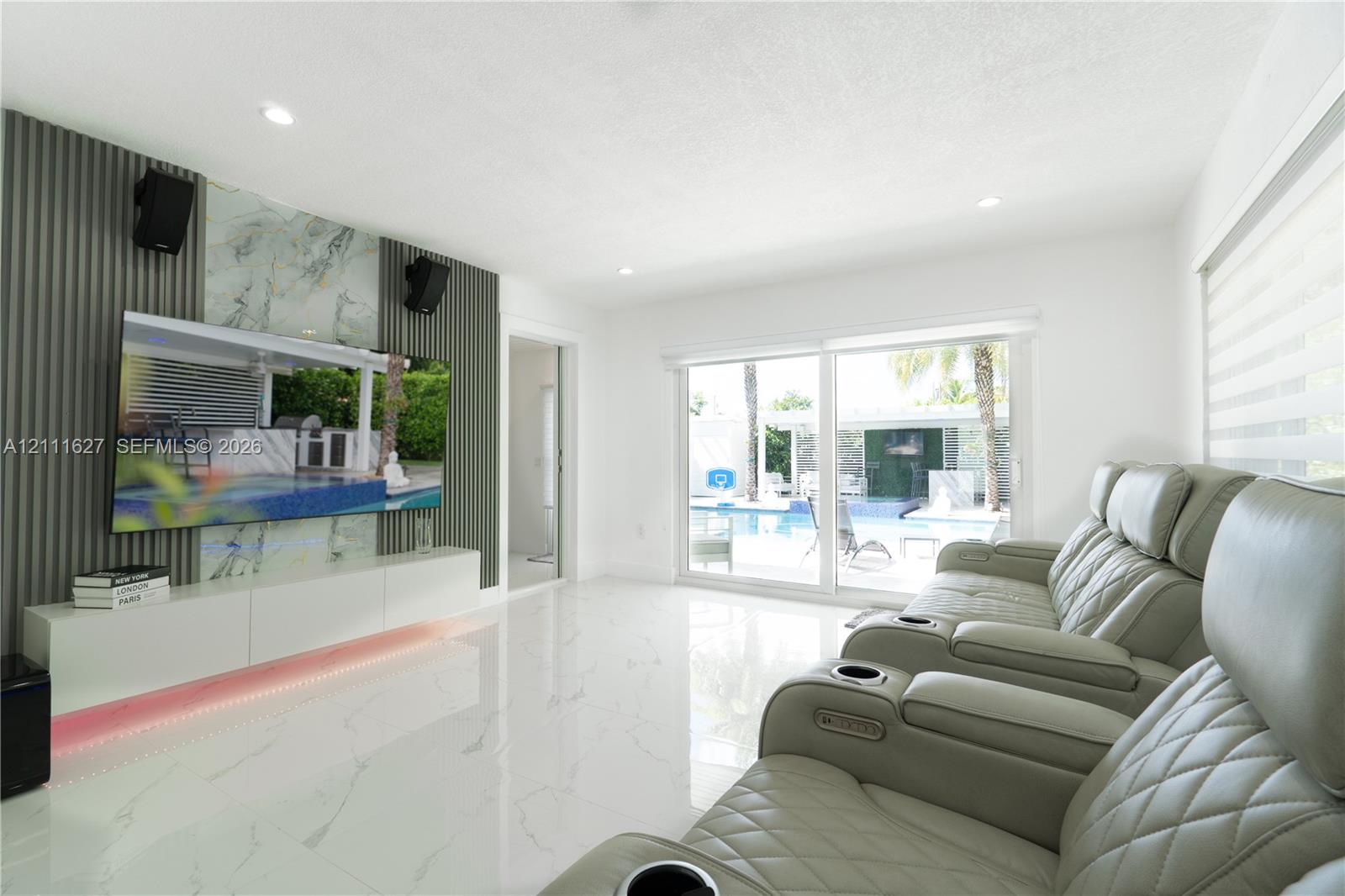 Polished stone-finish flooring, custom accent wall featuring vertical slats and a natural stone-finish inset, integrated low-profile cabinetry with under-cabinet lighting, and expansive sliding glass doors