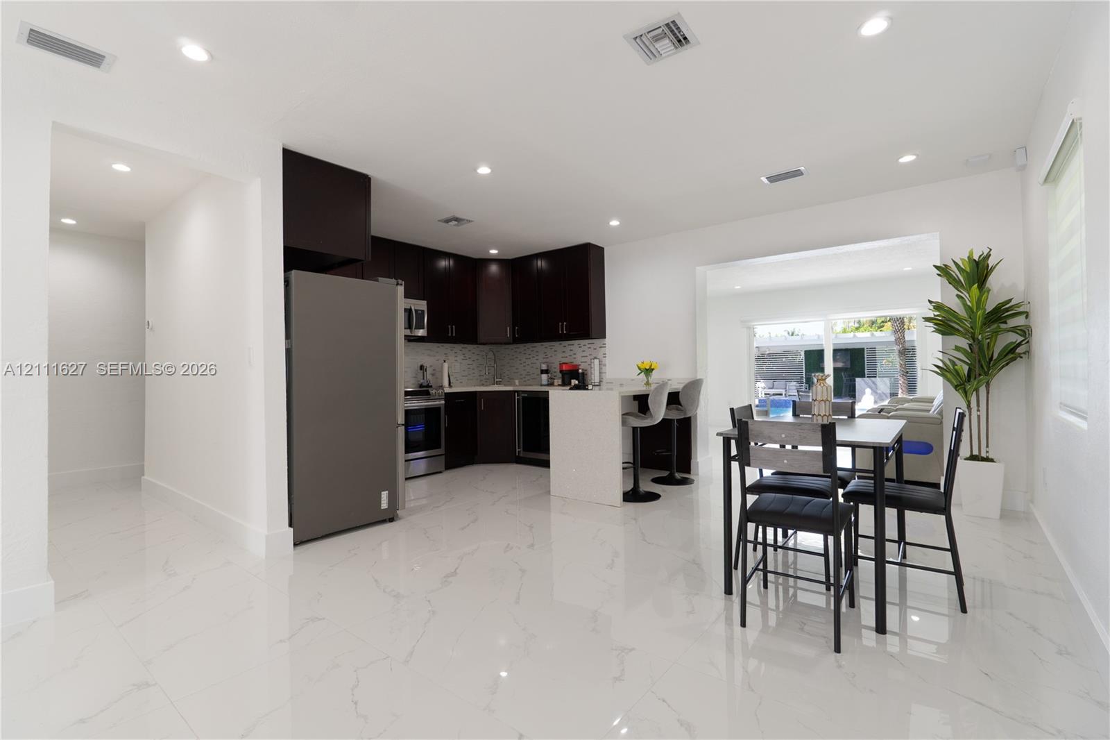 Kitchen featuring dark-toned cabinetry, a stone-finish countertop island with a breakfast bar, stainless steel appliances, a mosaic-tile backsplash, and polished stone-finish flooring