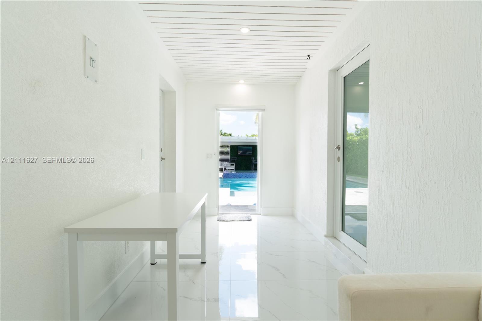 Hallway featuring white stone-finish flooring, slatted wood-paneled ceiling, and a full-height glass door