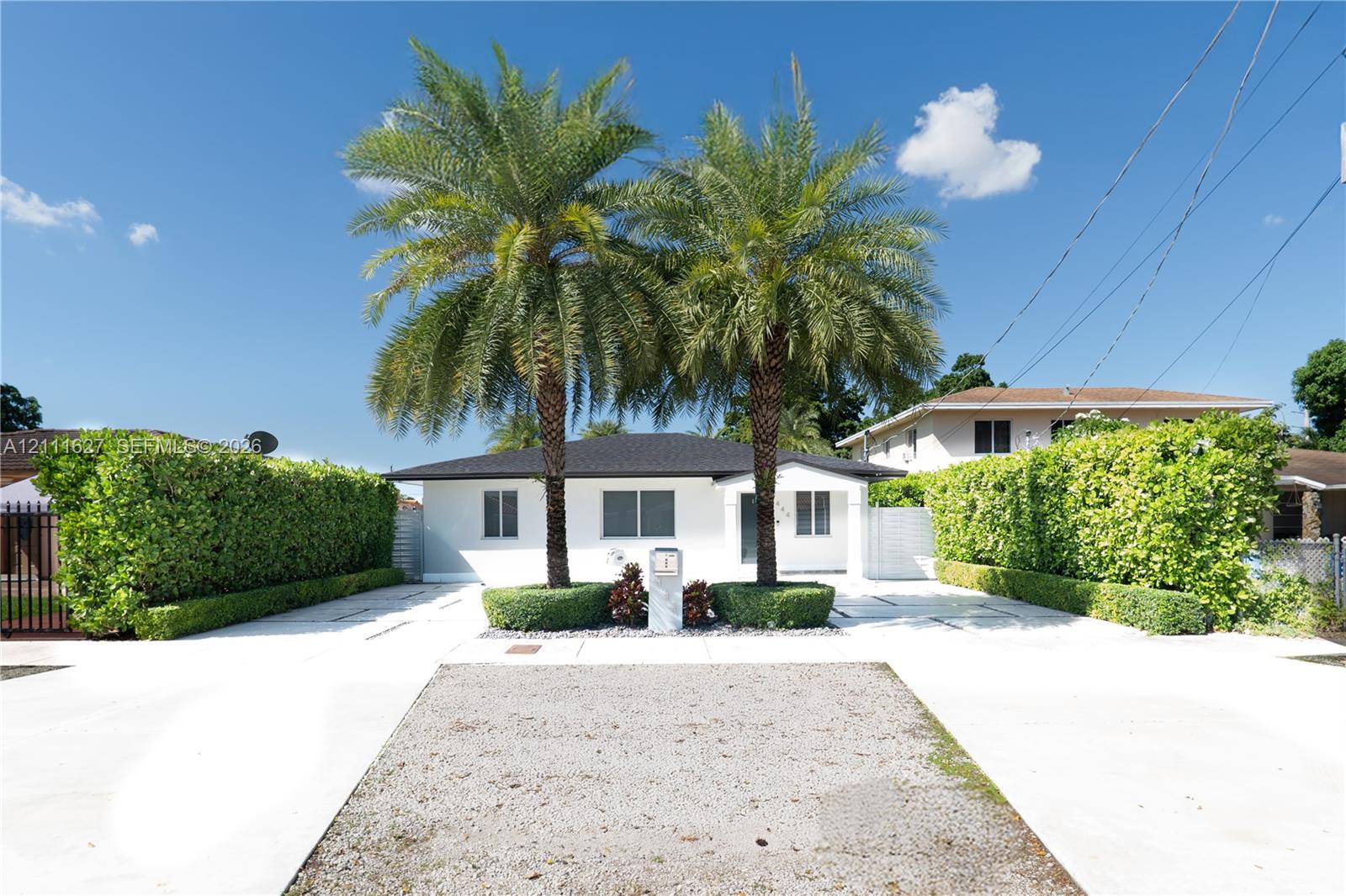 Single-story residence featuring a white exterior, hip roof, mature palm trees, and manicured privacy hedges Single-story residence featuring a white exterior, hip roof, mature palm trees, and manicured privacy hedges