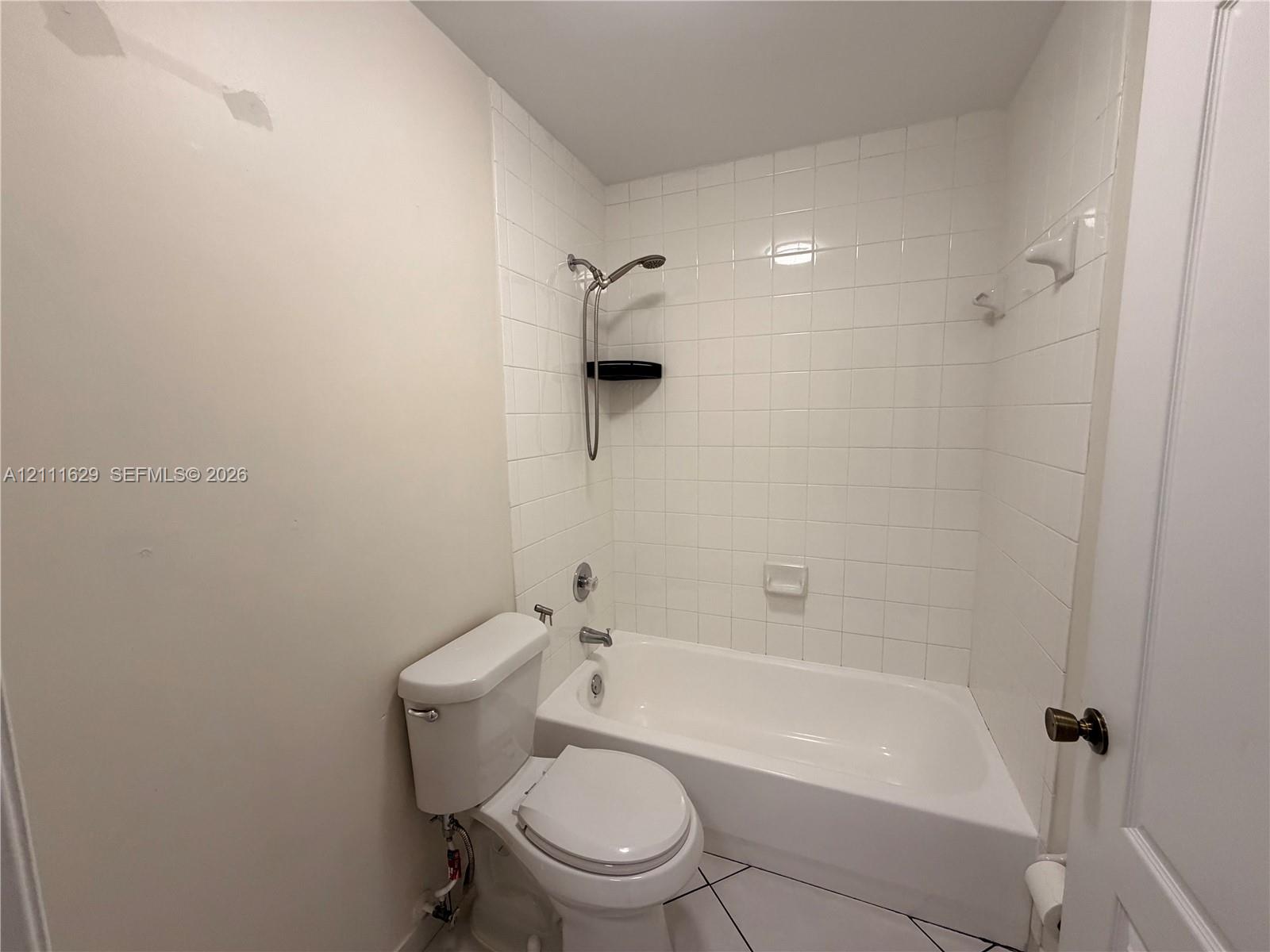 Bathroom featuring a porcelain tub and shower combination with white wall tile, a ceramic toilet, and tile flooring