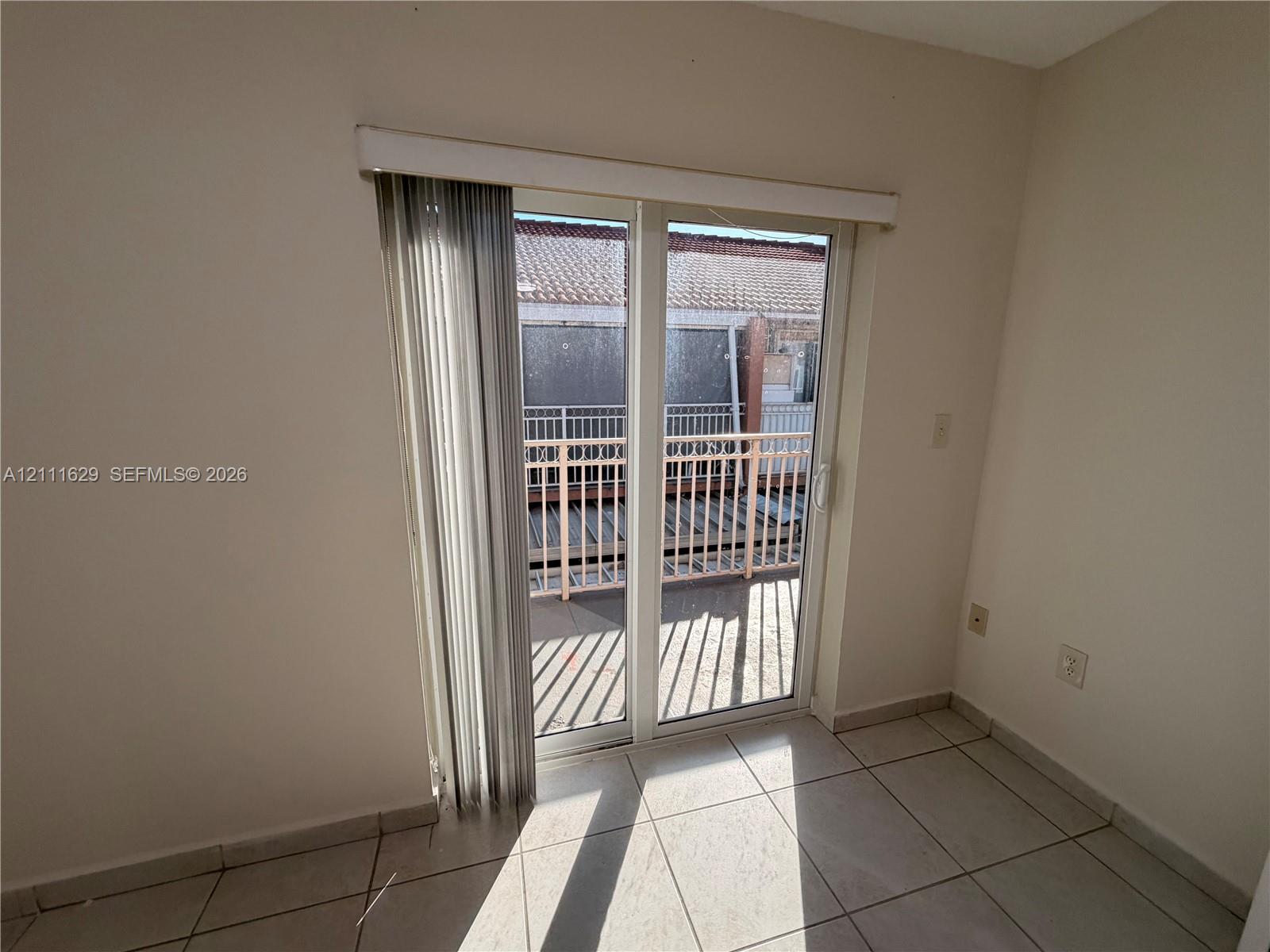 Double sliding glass doors with vertical blinds, tile flooring, and access to a balcony with metal railing