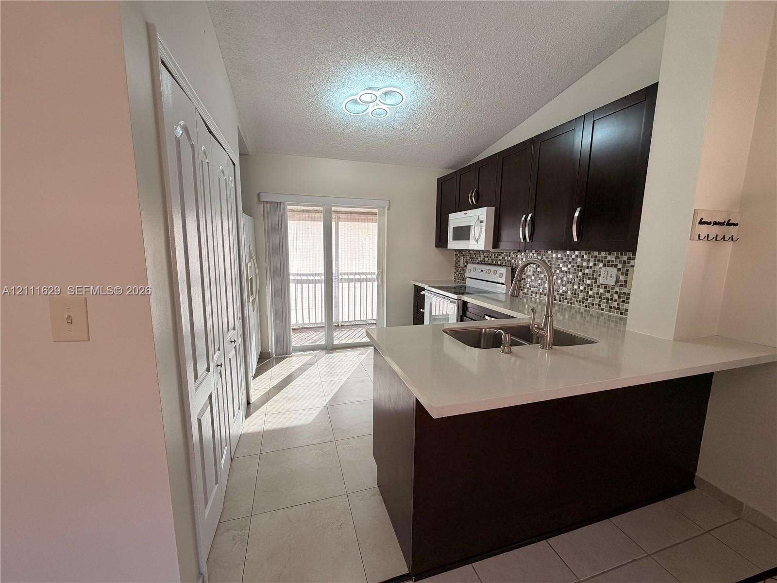 Kitchen featuring dark cabinetry, quartz countertops, mosaic tile backsplash, double-basin stainless steel sink with pull-down faucet, and tile flooring