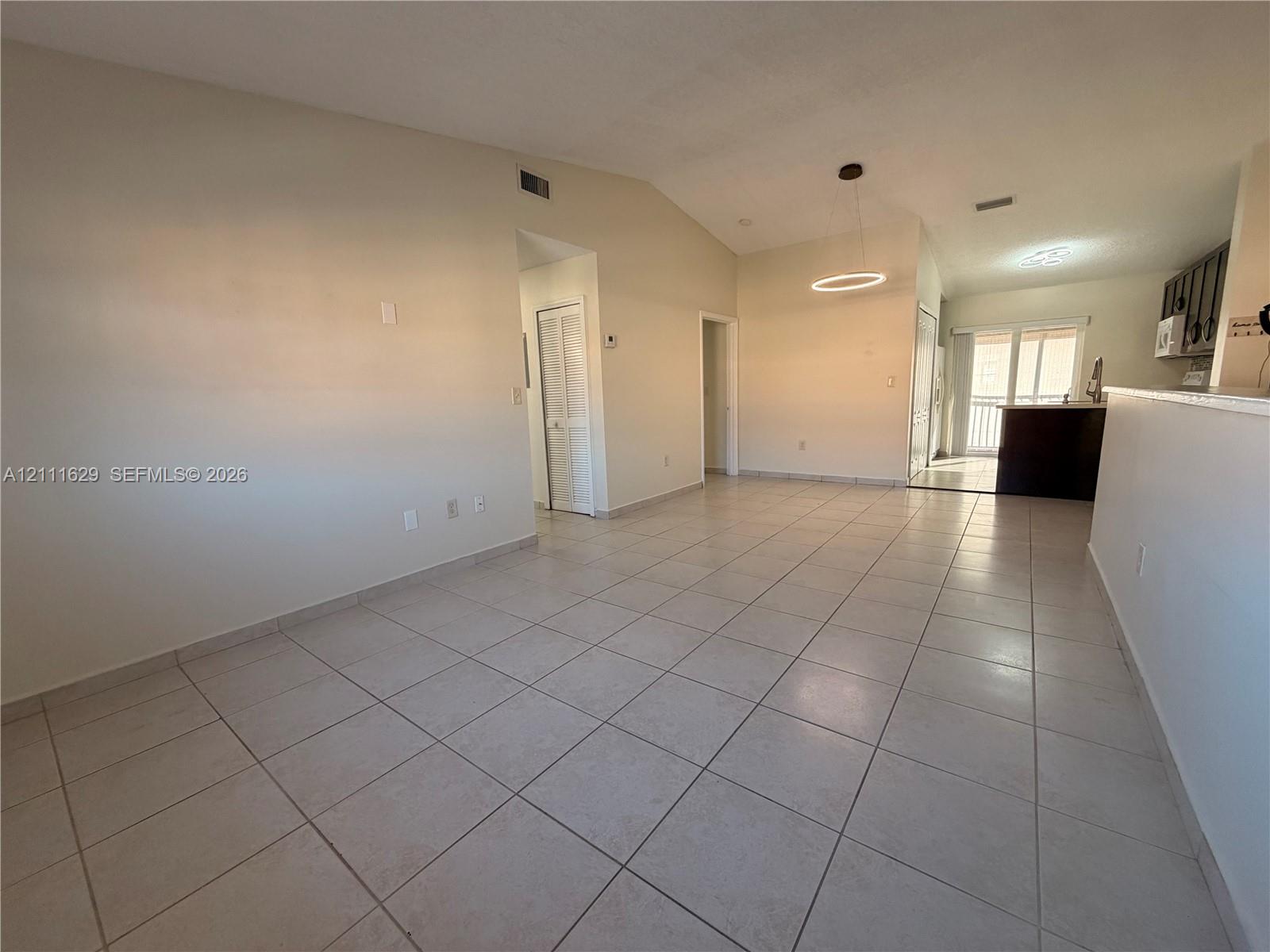Vaulted ceiling, ceramic tile flooring, modern circular pendant lighting, and neutral wall tones