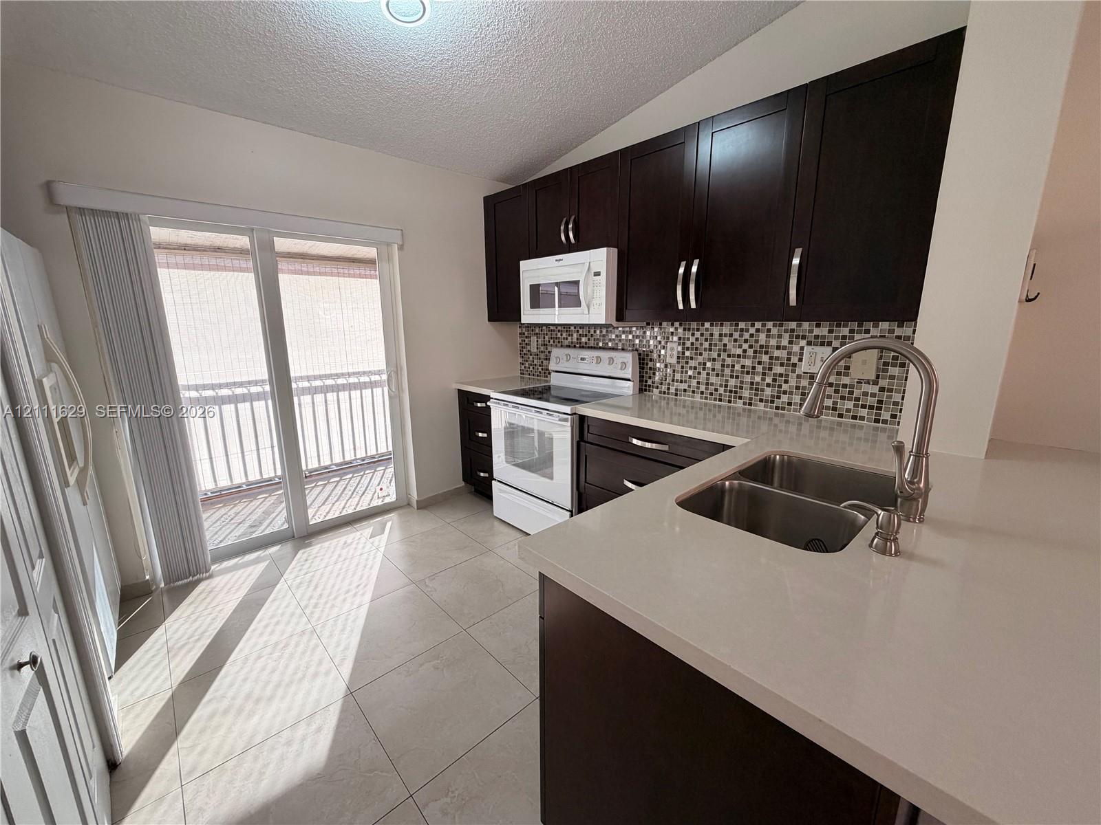 Kitchen featuring dark cabinetry, quartz countertops, a mosaic tile backsplash, a dual-basin stainless steel sink with a high-arch faucet, and porcelain tile flooring