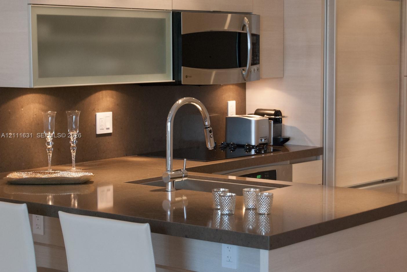 Kitchen featuring wood-finish cabinetry, quartz countertops, a stainless steel undermount sink with a gooseneck faucet, and an integrated stainless steel microwave Kitchen featuring wood-finish cabinetry, quartz countertops, a stainless steel undermount sink with a gooseneck faucet, and an integrated stainless steel microwave