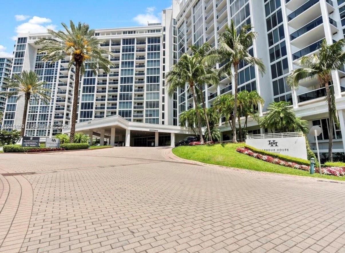 Multi-story high-rise exterior featuring a covered porte-cochre, paver driveway, expansive glass balconies, and manicured landscaping Multi-story high-rise exterior featuring a covered porte-cochre, paver driveway, expansive glass balconies, and manicured landscaping