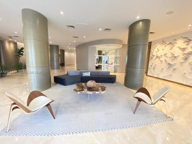 Open-concept lobby featuring polished stone flooring, curved architectural pillars, recessed lighting, and a textured decorative feature wall Open-concept lobby featuring polished stone flooring, curved architectural pillars, recessed lighting, and a textured decorative feature wall