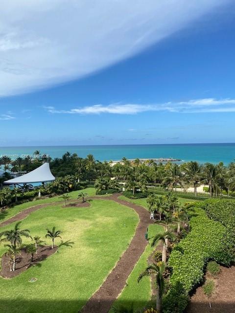 Expansive grounds featuring manicured turf, mature palm trees, meandering garden paths, and an ocean horizon backdrop