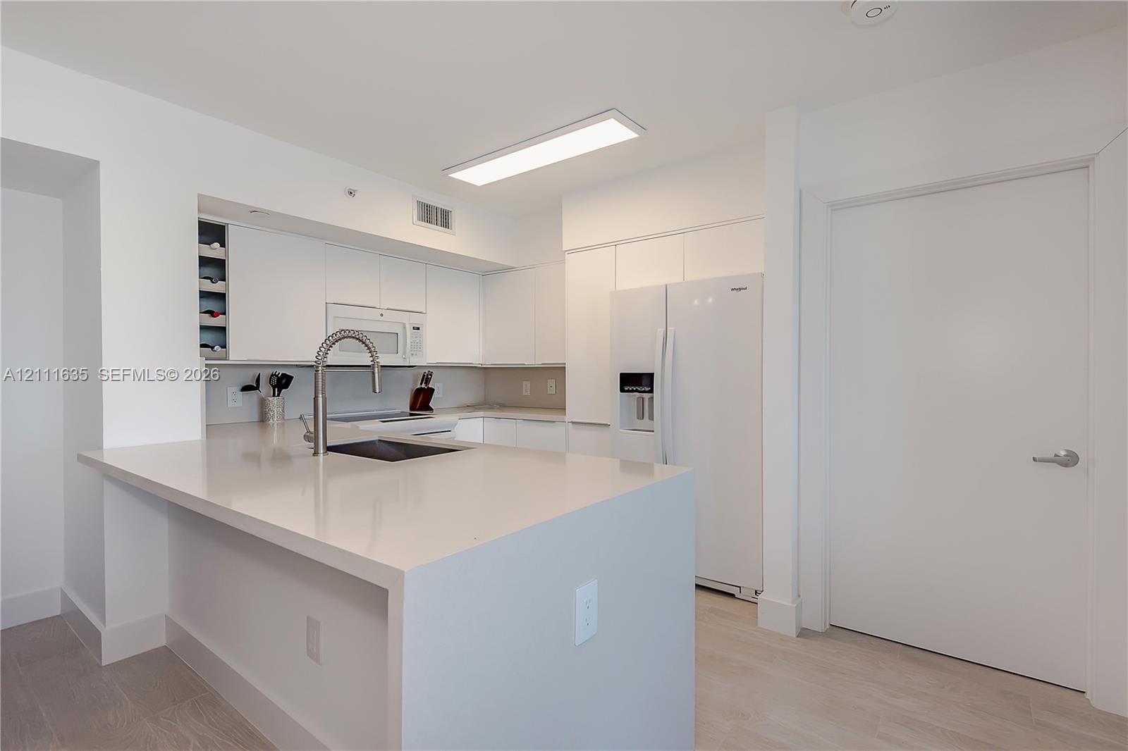 Kitchen featuring flat-panel white cabinetry, solid surface countertops, built-in wine rack, integrated microwave, and wood-finish flooring
