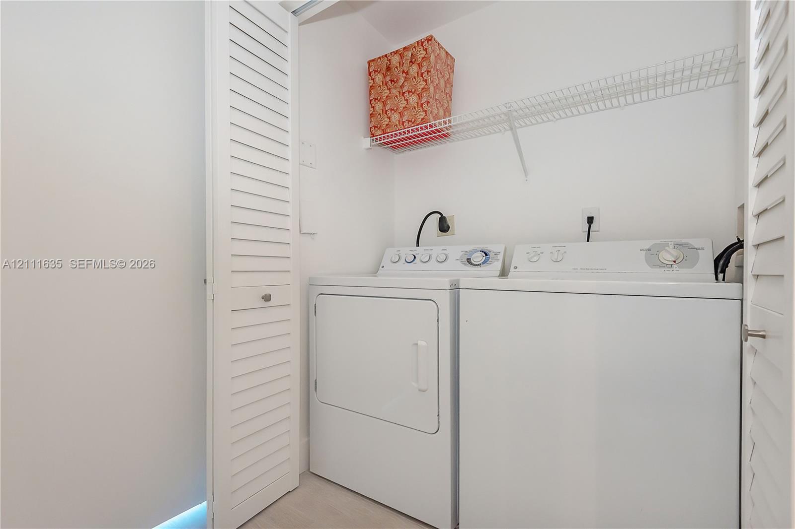 Laundry closet featuring white louvered doors, wire shelving, and dedicated hookups for a washer and dryer