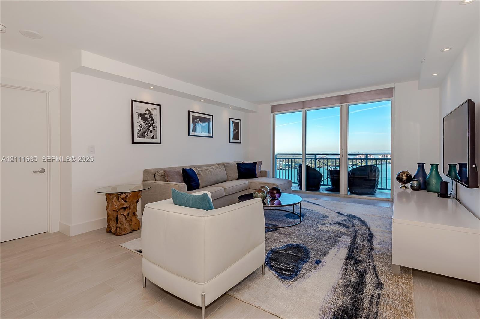 Living area featuring light-toned flooring, recessed ceiling lighting, and floor-to-ceiling glass panel doors opening to a balcony with metal railings Living area featuring light-toned flooring, recessed ceiling lighting, and floor-to-ceiling glass panel doors opening to a balcony with metal railings