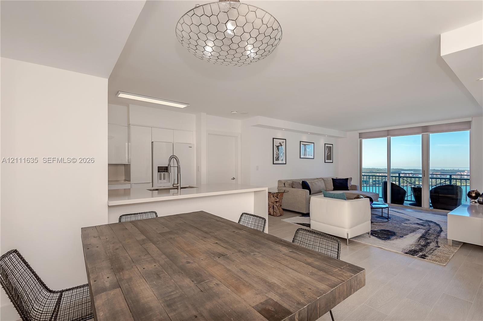 Open-concept floor plan featuring a kitchen with a white quartz breakfast bar, stainless steel faucet, and recessed lighting, finished with tile flooring and a geometric ceiling pendant